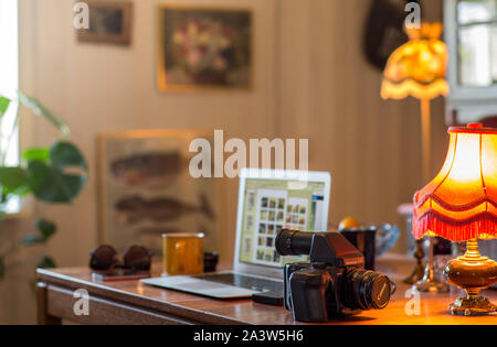 Vue d'un bureau à domicile avec une caméra analogique format moyen sur une table en face d'un ordinateur portable et autres objets divers. Banque D'Images