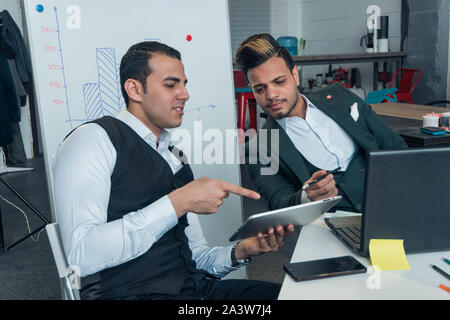 Deux jeunes hommes dans les complets sont à négocier et à la recherche à but lucratif d'affaires graphiques dans une tablette Banque D'Images