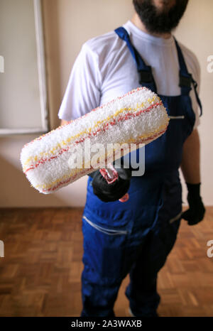 Travailleur de la construction au chantier de construction, uniforme de protection avec l'outil de service, de l'équipement. Il est titulaire d'rouleau à peindre brosse pour peinture murale. Banque D'Images