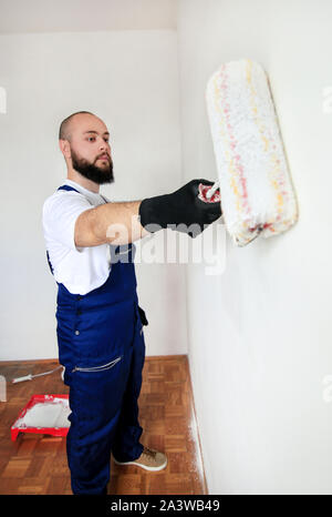 Travailleur de la construction de faire terminer la rénovation à l'appartement. Entrepreneur peintre professionnel à l'aide de la brosse de peinture blanche peinture de mur de béton. Banque D'Images