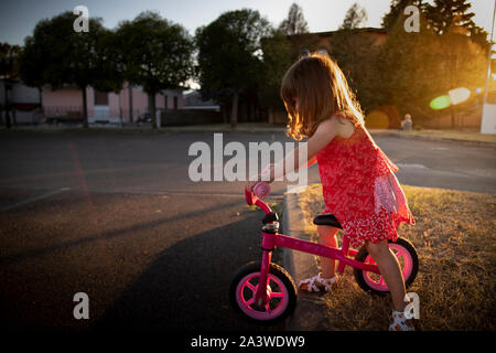 Tout-petit enfant girl riding son vélo urbain dynamique en extérieur avec la lumière au coucher du soleil d'or