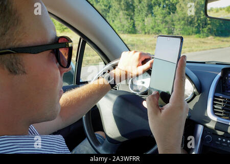 Un jeune homme regarde le téléphone au cours d'une approche dangereuse. À l'aide d'un téléphone dans une voiture texter au volant concept pour danger de message texte et d'être Banque D'Images