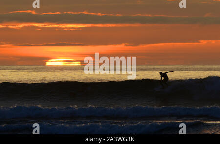 Un surfeur découpé sur le coucher de soleil comme ils montent une vague à Barvas Bay, sur la côte atlantique de l'île de Lewis, en Écosse. Banque D'Images