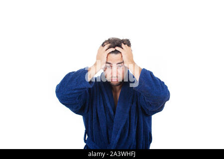 Portrait de jeune homme en retard porte peignoir bleu tenant la main à la tête, incapable de se réveiller à temps pour se rendre au travail, isolé sur fond blanc. Banque D'Images