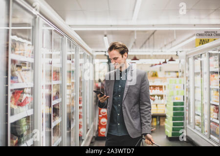 Man looking at smartphone dans une épicerie Banque D'Images