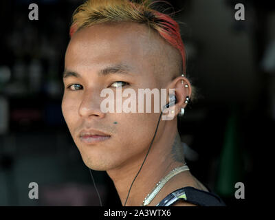 À la cool, jeune homme birman avec écouteurs, les cheveux teints et coupe de cheveux élégante pose pour la caméra. Banque D'Images