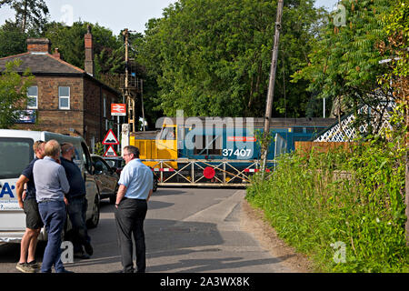 Pause sur la circulation le passage à niveau de la gare Brundall, Norfolk, Royaume-Uni. Une locomotive diesel de la classe 37 passe le passage à niveau. Banque D'Images