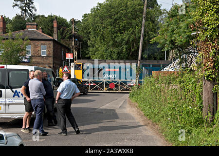 Pause sur la circulation le passage à niveau de la gare Brundall, Norfolk, Royaume-Uni. Une locomotive diesel de la classe 37 passe le passage à niveau. Banque D'Images