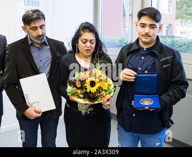 Hanau, Allemagne. 10 Oct, 2019. Ejder Sözen (l-r), le père, Yasemin Sözen, mère, et Ardar Sözen, frère, tenir ensemble après la présentation de la plaque d'honneur. Pour commémorer Alptug Sözen, une plaque d'honneur a été présenté à la ville de Hanau et une plaque commémorative a été dévoilée dans le Ludwig-GeiSSler-Schule. Le 17-year-old Hanauer était mort en novembre 2018 à la station de S-Bahn/Frankfurt-Main Ostendstraße, lorsqu'il a voulu aider une personne sans-abri ivre qui était couché sur les voies. Crédit : Andreas Arnold/dpa/Alamy Live News Banque D'Images