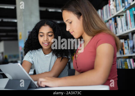 Les étudiantes du secondaire étudiant with digital tablet in library Banque D'Images