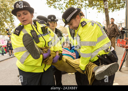 Trafalgar Square, Londres, Royaume-Uni. 10 octobre 2019. Un groupe de policiers britanniques vêtus de vestes de haute visibilité transportent un individu enveloppé dans une couverture ou un manteau brun lors d'une manifestation ou d'une manifestation publique. Les policiers portent des chapeaux noirs avec des bandes à carreaux et portent des radios et du matériel. La scène se déroule à l'extérieur, avec des arbres et des passants visibles en arrière-plan, suggérant une intervention policière dans un espace public. Scènes autour de Trafalgar Square alors que la protestation contre l'extinction de la rébellion entre dans son quatrième jour. Penelope Barritt/Alamy Live News Banque D'Images