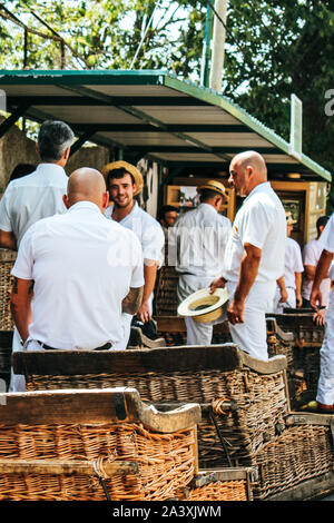 Monte, Madeira, Portugal - 14 Sep 2019 : panier en osier des luges, pilotes, trouble Carreiros do Monte. en arrière-plan. Transport traditionnel pour Funchal, maintenant attraction touristique. Les chapeaux de paille, des vêtements blancs. Banque D'Images