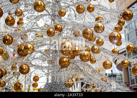 Arbre de Noël artificiel inhabituel fait de métal tressé branches ampoules par garland avec billes jaunes au centre de la ville Banque D'Images