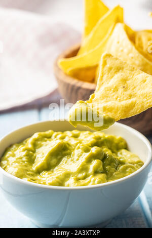 Croustilles de maïs et d'avocat trempette. Croustilles de maïs jaune et de guacamole en cuvette sur tableau bleu. Banque D'Images