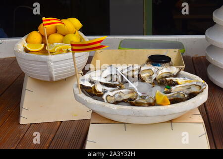 Assiette pleine d'huîtres français pour la vente sur le marché local dans le centre-ville. Bol plein de tranches de citron et les drapeaux Catalan standing out. Banque D'Images