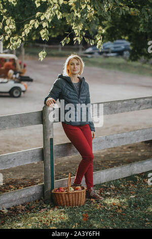 Portrait de la belle race blanche d'âge moyen aux cheveux courts blond woman standing by clôture en bois sur ferme avec panier en osier. Personne recueillir pic de récolte Banque D'Images