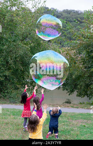 Groupe de jeunes enfants chasse et tente de prendre des bulles géantes. Banque D'Images