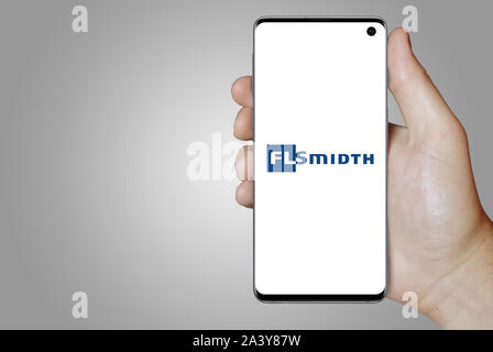 Un homme est titulaire d'un téléphone d'afficher le logo de société FLSmidth & Co. énumérés sur OMX Copenhagen. Fond dégradé de gris. Credit : PIXDUCE Banque D'Images