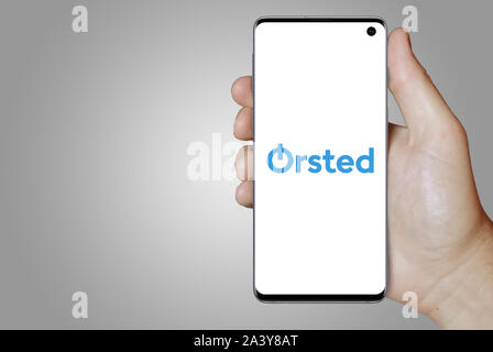 Un homme est titulaire d'un téléphone d'afficher le logo de société Ørsted énumérés sur OMX Copenhagen. Fond dégradé de gris. Credit : PIXDUCE Banque D'Images