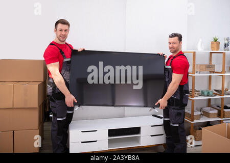 Deux hommes en uniforme des déménageurs professionnels le déchargement d'une TV LCD dans le salon Banque D'Images