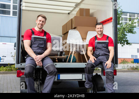 Portrait Of Smiling Movers assis en Van avec pile de cartons et de meubles Banque D'Images