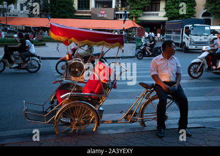 Dans une rue du Vieux quartier de Hanoi, Vietnam, un chauffeur attend que quelqu'un se prenne dans les couleurs du coucher du soleil. Banque D'Images