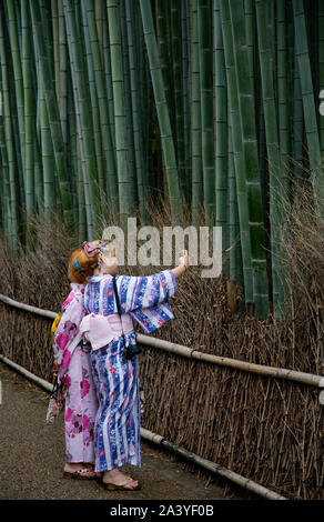Deux jolies filles dans les kimonos d'été (yukata) aiment prendre un selfie lors d'une visite dans la forêt de bambou à côté du temple Tenryu-ji. Kyoto, Japon. Banque D'Images