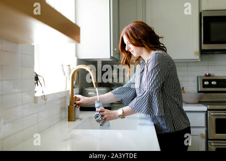 Femme d'eau de remplissage bouteille dans l'évier de cuisine Banque D'Images