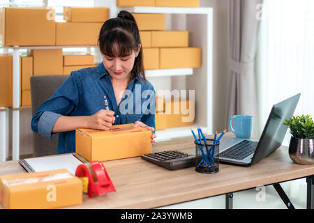 Charmante belle asiatique propriétaire adolescent femme d'affaires travailler à la maison pour faire des achats en ligne, l'écriture adresse en boîte aux lettres avec un ordinateur portable avec l'équipement de bureau, Banque D'Images