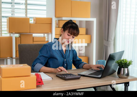 Charmante belle asiatique propriétaire adolescent femme d'affaires travailler à domicile pour le magasinage en ligne, calculer le prix des marchandises avec un ordinateur portable avec l'équipement de bureau, e Banque D'Images