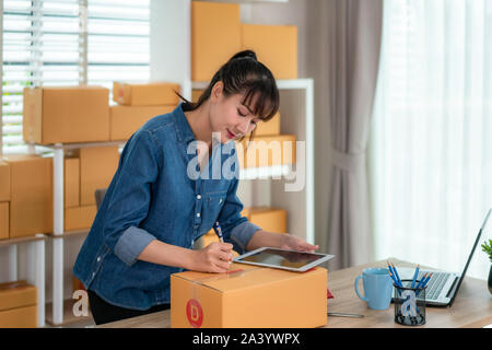 Charmante belle asiatique propriétaire adolescent femme d'affaires travailler à la maison pour faire des achats en ligne, l'écriture adresse en boîte aux lettres avec un ordinateur portable avec l'équipement de bureau, Banque D'Images