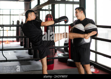 Young Asian kick boxer coups formateur professionnel dans la boxe à l'arrière-plan studuim au fitness. La Une de l'Boxer sac de sable pour le culturisme Banque D'Images