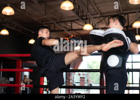 Young Asian kick boxer coups formateur professionnel dans la boxe à l'arrière-plan studuim au fitness. La Une de l'Boxer sac de sable pour le culturisme Banque D'Images