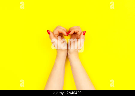 Nails design. Deux belle femme avec les mains manucure rouge ressemblent à cœur sur fond jaune. Place pour le texte. Banque D'Images