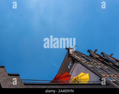 Parasols rouge et jaune sur un balcon élevé contre le ciel bleu et un avion volant au-dessus du vrai high Banque D'Images