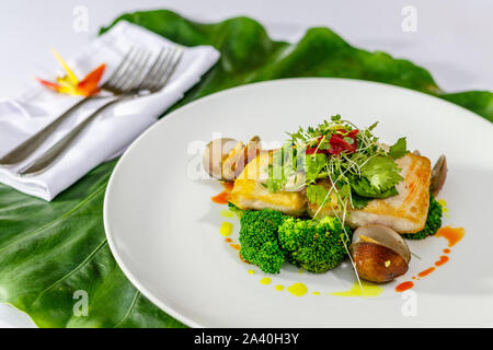 Plaque en céramique blanche avec filet de mahi-mahi et les palourdes avec le brocoli, l'oignon, persil et fèves germées servi sur une feuille verte. Vue d'en haut Banque D'Images