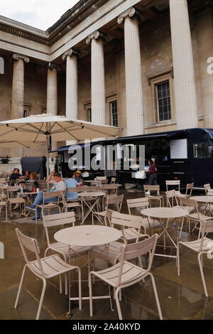 Les gens s'asseoir sous un parasol à un café extérieur à proximité d'un camion alimentaire au British Museum de Londres, Royaume-Uni, en début d'été. Banque D'Images