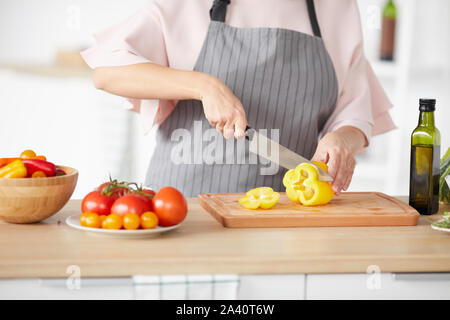 Close-up of woman in apron cutting poivre à l'aide d'un couteau sur une planche à découper pour la salade Banque D'Images