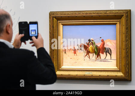 Londres, Royaume-Uni. 11 octobre 2019. Un visiteur photographies 'Riders Traversée du désert', 1870, par Jean-Léon Gérôme, (Est) m3-5GBP. Essai d'œuvres de la collection de peintures orientalistes Najd chez Sotheby's à New Bond Street, qui enregistrent la vie quotidienne dans le quartier historique, arabe et islamique Ottoman tous les 155 peintures sont à la vue du public 11- 15 octobre, avec 40 oeuvres qui seront mises aux enchères le 22 octobre. Crédit : Stephen Chung / Alamy Live News Banque D'Images