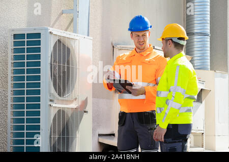 Deux électriciens hommes portant des vestes de sécurité Contrôle de l'unité de climatisation sur le toit du bâtiment Banque D'Images