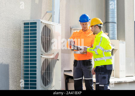 Deux électriciens hommes portant des vestes de sécurité Contrôle de l'unité de climatisation sur le toit du bâtiment Banque D'Images