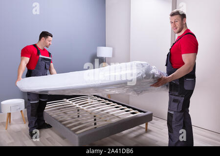 Deux hommes en uniforme des déménageurs professionnels de placer le matelas sur le lit dans la nouvelle maison Banque D'Images