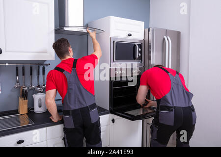 Deux techniciens du sexe masculin la fixation du capot d'échappement et un four dans la cuisine modulaire Banque D'Images