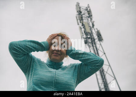 La femme tient sa tête près de la BTS. Rayonnement nocif des réseaux cellulaires 5G network concept transmetteurs Banque D'Images