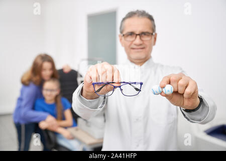 Focus sélectif de nouvelles lunettes et qualitatives pour une meilleure vision de la lentille optique en magasin. Oculiste mâle looking at camera, tout en offrant aux clients de lunettes à l'arrière-plan. Concept de correction de la vue. Banque D'Images