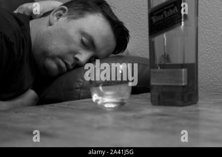 Un homme évanoui sur le canapé de dormir à côté d'une bouteille de whisky Johnnie Walkers étiquette bleue et un verre de whisky vide Banque D'Images