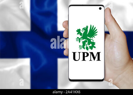 Un homme est titulaire d'un téléphone d'afficher le logo de société UPM-Kymmene énumérés sur OMX Helsinki. Drapeau d'arrivée. Credit : PIXDUCE Banque D'Images