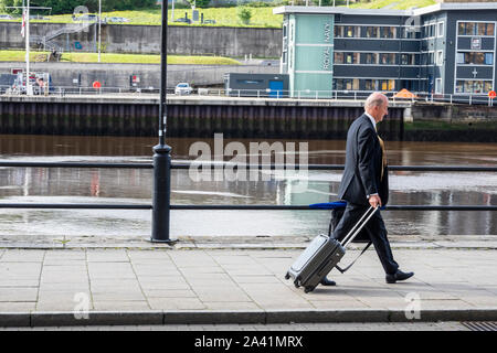 Un homme d'âge moyen avec une valise à roulettes à pied le long des quais à Newcastle Upon Tyne, Tyne and Wear, England, UK Banque D'Images