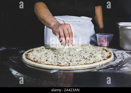 Mettre la main des chefs fromage sur la pizza à fond noir. Banque D'Images