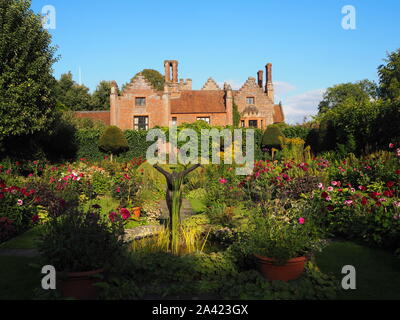 Chenies Manor House sur une soirée de fin d'été, jardin en contrebas dahlias, chemins d'herbe et de plantes border.bassin d'agrément avec statue d'atteindre le haut. Banque D'Images